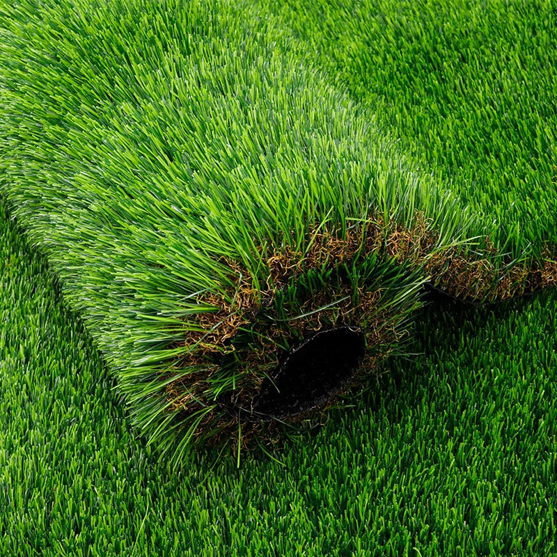 Close-up of artificial grass blades and brown thatch around a rolled edge.